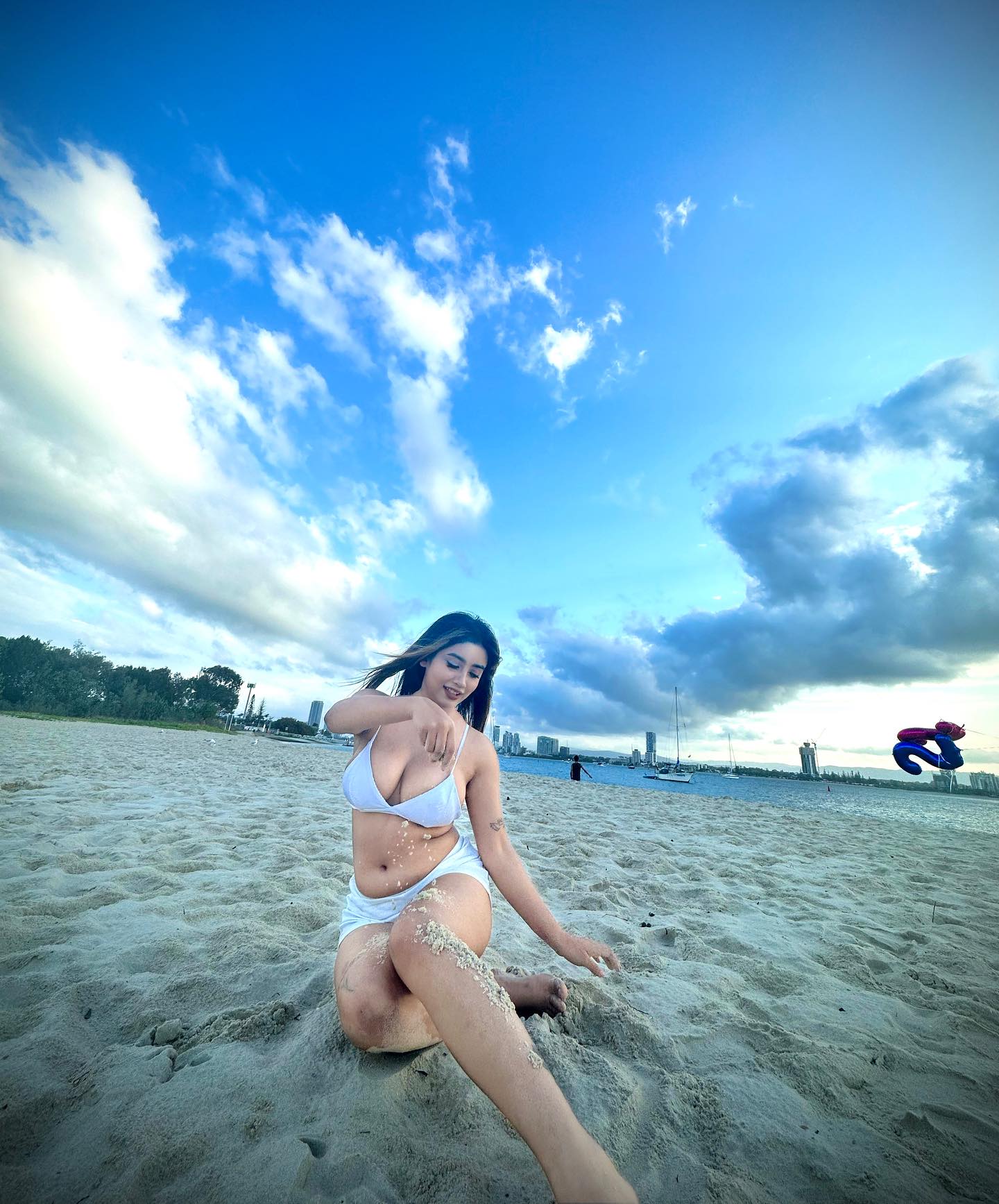Sandhya in white bikini on the beach with dramatic blue sky